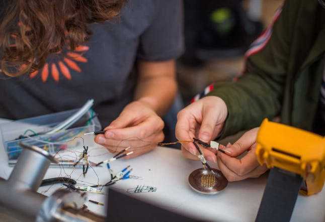 A close-up image of two people's hands as they do electrical work at a table.